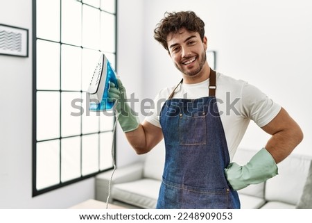 Young hispanic man doing chores holding iron machine at home