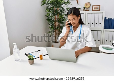 Young latin woman wearing doctor uniform talking on the smartphone at clinic