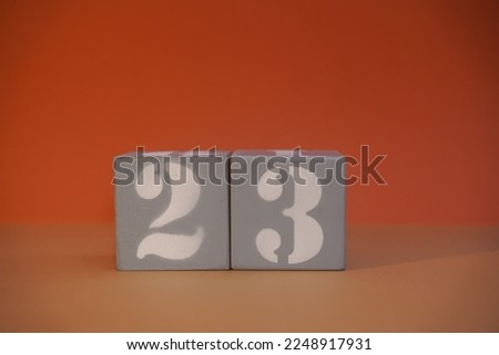 Number 23 on wooden grey cubes close-up. Concept of date time. Math concept. Copy space for text or event. White numbers 23 on building blocks, orange background. Educational cubes. Selective focus