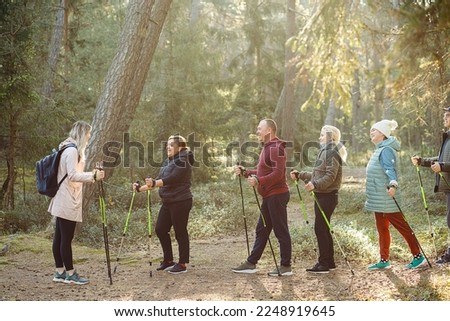 Blond woman coach, sports trainer with group of people teach Scandinavian, Nordic walking exercises with sticks in the forest, nature. Healthy way of life. Exercises hiking education for team people.  Royalty-Free Stock Photo #2248919645