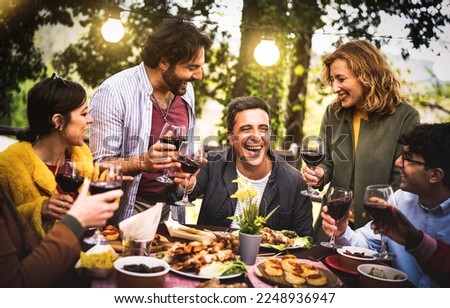 Young men and women having fun drinking out at wine diner - Food and beverage life style concept on mixed age people enjoying time together at villa patio - Warm filter with bulb string lights halo Royalty-Free Stock Photo #2248936947