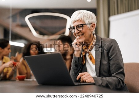 Senior woman working online, over the laptop while sitting in the office with her colleagues. Royalty-Free Stock Photo #2248940725