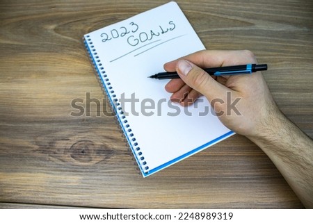 My 2023 goals list written on white paper over wooden background and hand holding pen above the list.
