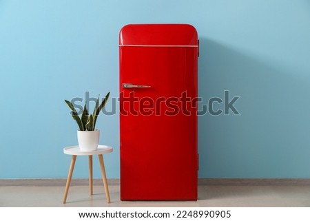 Stylish retro fridge and table with houseplant near blue wall