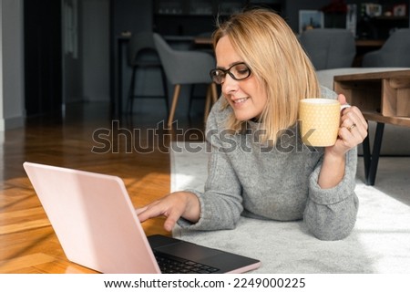 Full length photo of cheerful attractive young lady lie floor using laptop computer wear glasses good mood inside home indoors