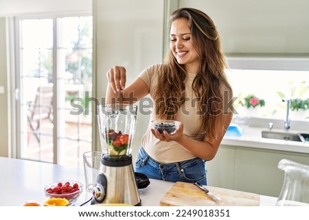 Young beautiful hispanic woman preparing vegetable smoothie with blender at the kitchen Royalty-Free Stock Photo #2249018351