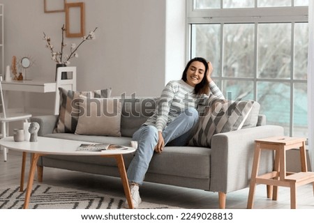 Young woman sitting on grey couch in living room Royalty-Free Stock Photo #2249028813