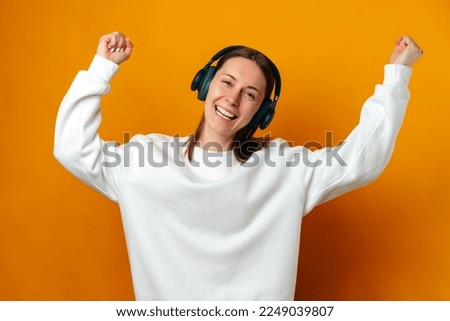 Young woman has fun while dancing and listening to the music in headphones over yellow background.