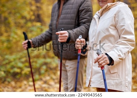 Cropped caucasian european couple in casual wear walking with nordic walking poles in autumn park. Elderly woman and old man with gray hair doing exercise outdoors. Healthy lifestyle concept. Royalty-Free Stock Photo #2249043565