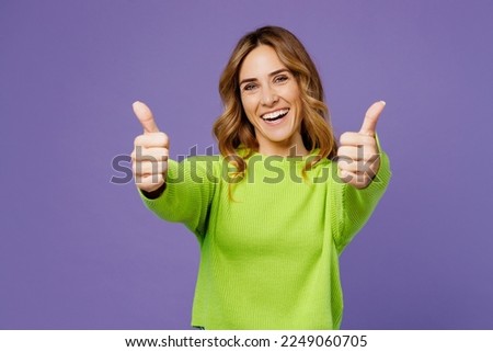 Young smiling fun cool positive woman 30s she wearing casual green knitted sweater showing thumb up like gesture isolated on plain pastel purple background studio portrait. People lifestyle concept