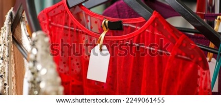 Elegant female clothes with blank paper tag in shop, closeup