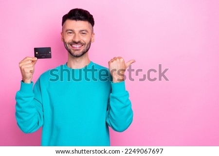 Photo of cheerful man toothy smile arm hold debit card indicate finger empty space isolated on pink color background