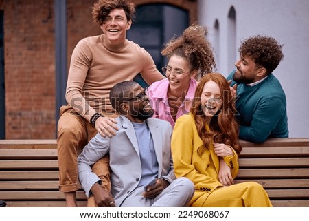 happy business executives talking in city park while taking coffee break on bench, having fun, laughing, talking jokes. attractive ladies and guys relaxing together, sitting on bench Royalty-Free Stock Photo #2249068067