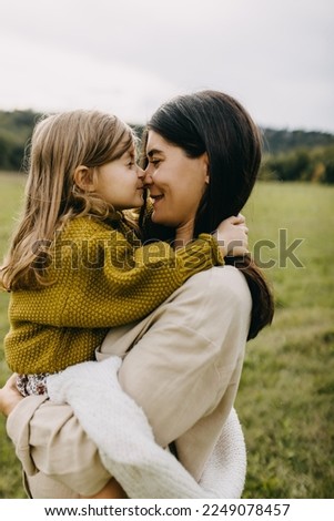 Closeup portrait of pregnant woman and her toddler daughter. Mother hugging little girl, holding in arms, touching noses.