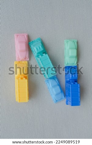 Horizontal framing of the letter N. This photography is a part of a conceptual image serial illustrating a sign or a letter using toy pastel colored plastic cars and trucks.