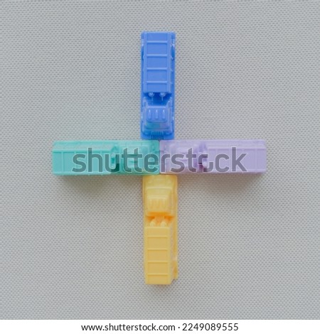 Horizontal framing of the addition sign +. This photography is a part of a conceptual image serial illustrating a sign or a letter using toy pastel colored plastic cars and trucks.