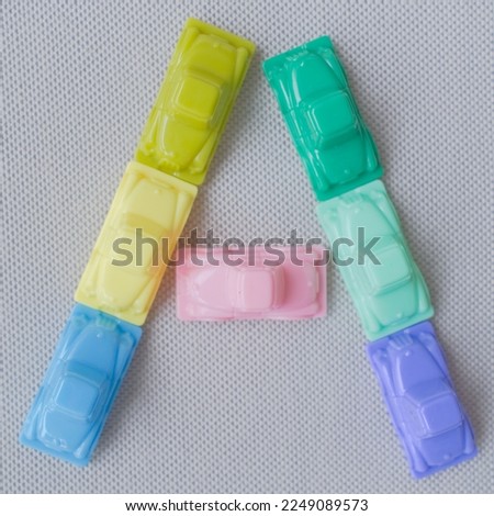 Horizontal framing of the letter A. This photography is a part of a conceptual image serial illustrating a sign or a letter using toy pastel colored plastic cars and trucks.