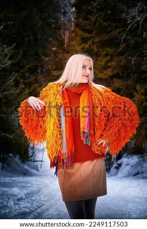 Outdoor portrait of blonde beautiful girl posing in snow in orange dress in winter day