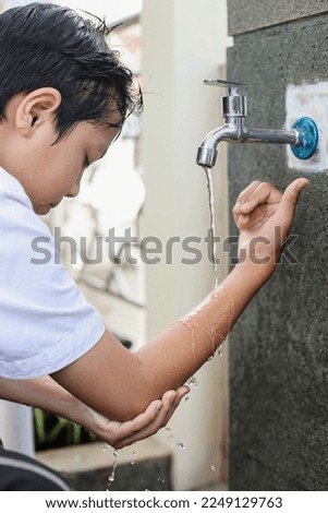 Side view of muslim kids washing right hand to elbow arms, ablution procedure before praying salah.  Royalty-Free Stock Photo #2249129763