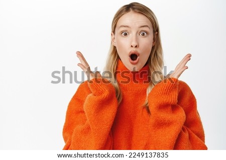 Excited cute blond girl looking surprised and amazed, gasping fascinated, reaction to big surprise, amazement and fascination, standing over white background