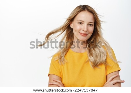 Beauty and haircare. Attractive young woman with natural blond hair waving flying in air, looking stunning at camera, posing against white background in yellow t-shirt Royalty-Free Stock Photo #2249137847
