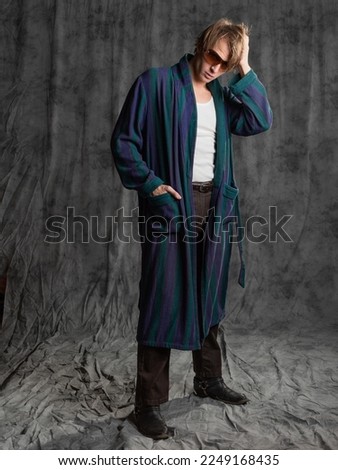 relaxed dude after a party in a housecoat with a shaggy head, posing in the studio on a gray background