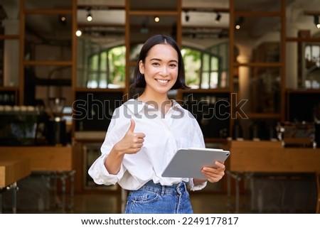 Young female entrepreneur, cafe manager standing with tablet and showing approval, recommending restaurant.