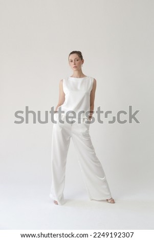 Serie of studio photos of young female model in all white silk outfit, sleeveless blouse and wide legs trousers	 Royalty-Free Stock Photo #2249192307