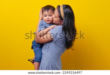 Portrait of happy young family. mother hugging and kissing son child isolated on yellow background. Mother's Day, parenthood, childhood concep