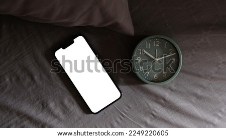 Alarm clock and mobile smart phone on bed in bedroom, waiting for phone call.