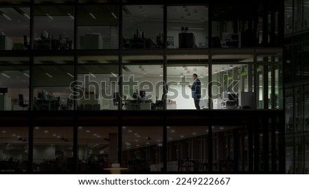 Man working late night in empty building with transparent glass window, modern Royalty-Free Stock Photo #2249222667