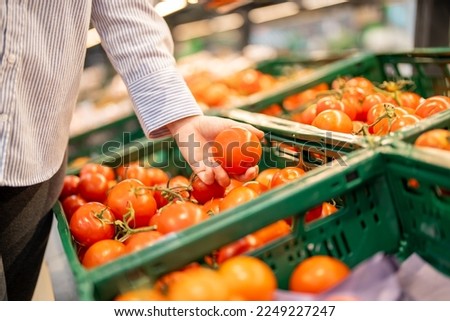 Customer choosing tomatoes in the supermarket.  Woman hand holding tomatoes in the market. Healthy lifestyle concept. Grocery shopping.