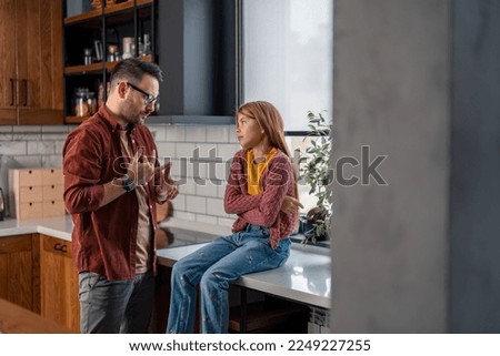 Displeased father having a conversation with his pensive daughter about her behavior, gesturing with hands, setting up the new home rules. Girl's sitting with the arms crossed and looking sadly at him Royalty-Free Stock Photo #2249227255