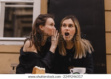 Gossiping. Two beautiful young women gossiping telling something on ear while sitting in the cafe. Communication and friendship concept. Young woman telling her friend some secrets. Royalty-Free Stock Photo #2249246317