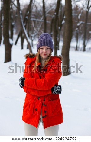 A young girl, blonde, in a sweater, hat and an orange jacket, against the backdrop of the winter landscape. Snow and frost, the concept of Christmas.