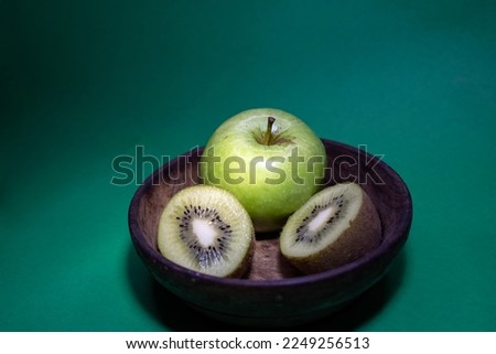 Green granny smith apple and green kiwi fruit slices in a wood bowl isolated on green background.