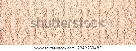 Knitted beige background. Large knitted fabric with a pattern. Close-up of a knitted blanket. Horizontal ornament. Banner