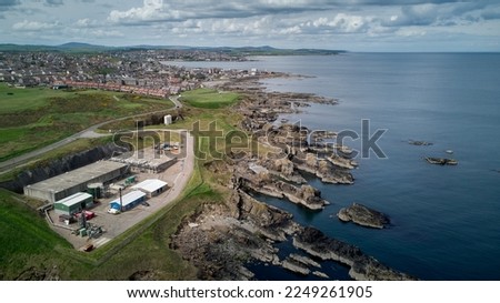 A drone photo of a rocky seaside with a Scottish town at a distance