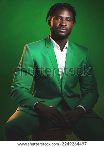 Fashion, formal and black man in a green suit sitting on a chair in studio with a luxury outfit. Elegant, stylish and portrait of an African male model with fashionable clothes isolated by background