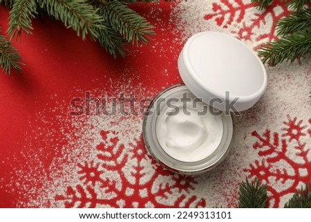 Winter skin care. Hand cream near snowflake silhouettes made with artificial snow and fir branches on red background, flat lay