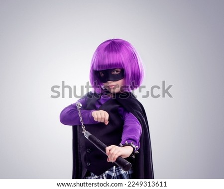 Kid, costume girl or vigilante in studio portrait with nunchaku, fantasy or creative comic clothes. Kid, superhero aesthetic, mask and creative for martial arts, villain or cosplay by gray background
