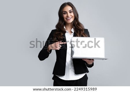 Woman holding laptop with empty mock up screen. Portrait of a young happy business woman with a laptop over gray background.