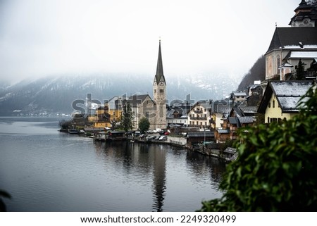 photo of Hallstatt a town by a lake in Europe in Austria, the photo was taken in December in winter time with landscapes covered in snow. With beautifull houses and sulcptures.