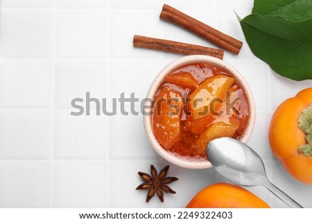 Bowl of tasty persimmon jam and ingredients on white tiled table, flat lay. Space for text