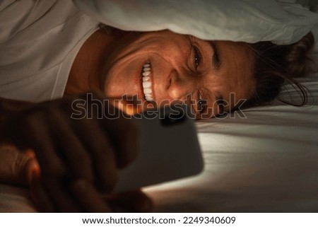 woman using smartphone under bedcover at night. Person looking at Online dating app with cell in dark home. Sexting or cheating concept image. 
