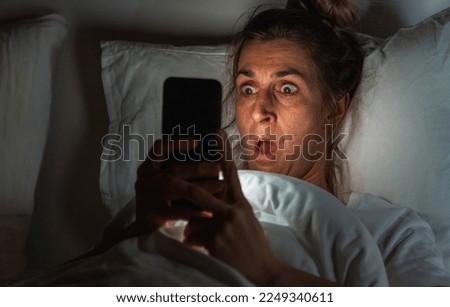 Shocked woman using smartphone in bed. Insomnia and stalking concept image