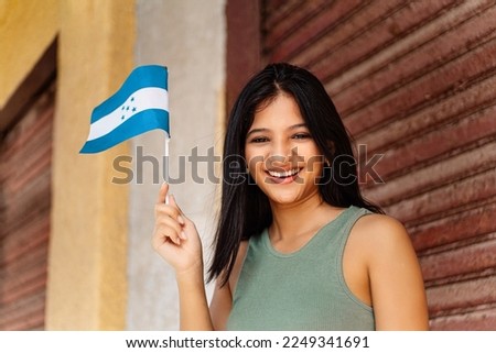 Young hispanic woman smilling holding and waving a small honduras flag.