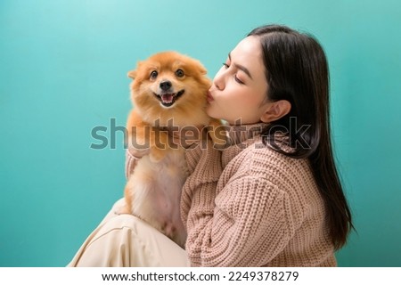 A Portrait of Young beautiful woman kisses and hugs her dog over green background.