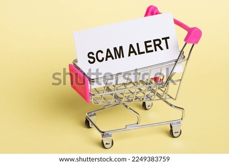 The inscription SCAM ALERT on a business card lying in a shopping cart on a yellow background