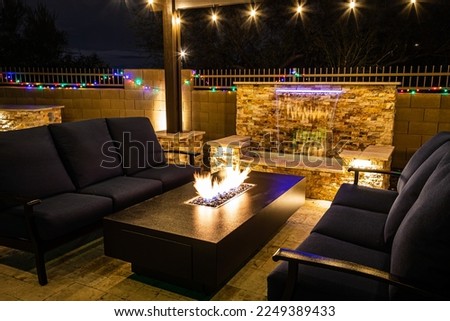 A resort style backyard at night with a waterfall, pergola, and a firepit at night.